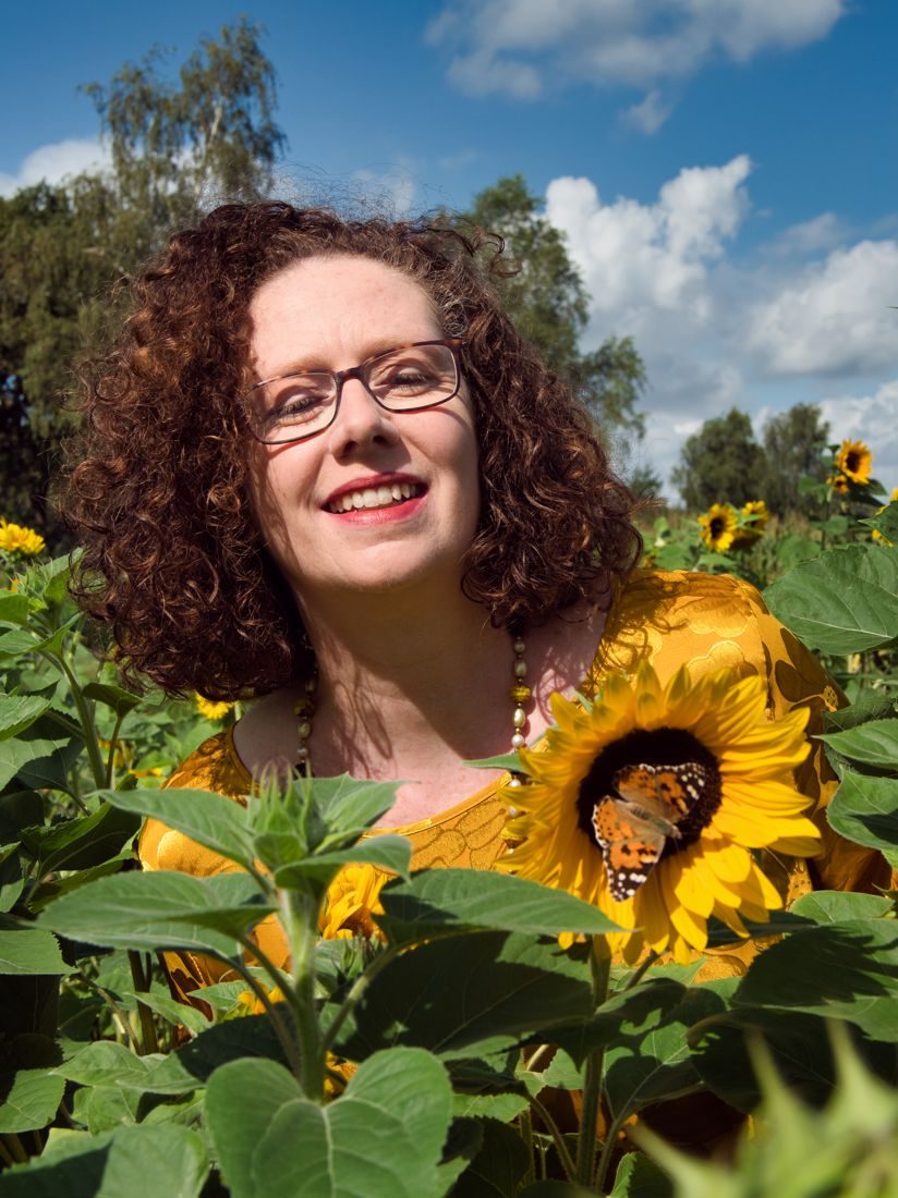 Sylvia Herdan im Sonnenblumenfeld, ein Schmetterling sitzt auf der Sonnenblume neben ihr